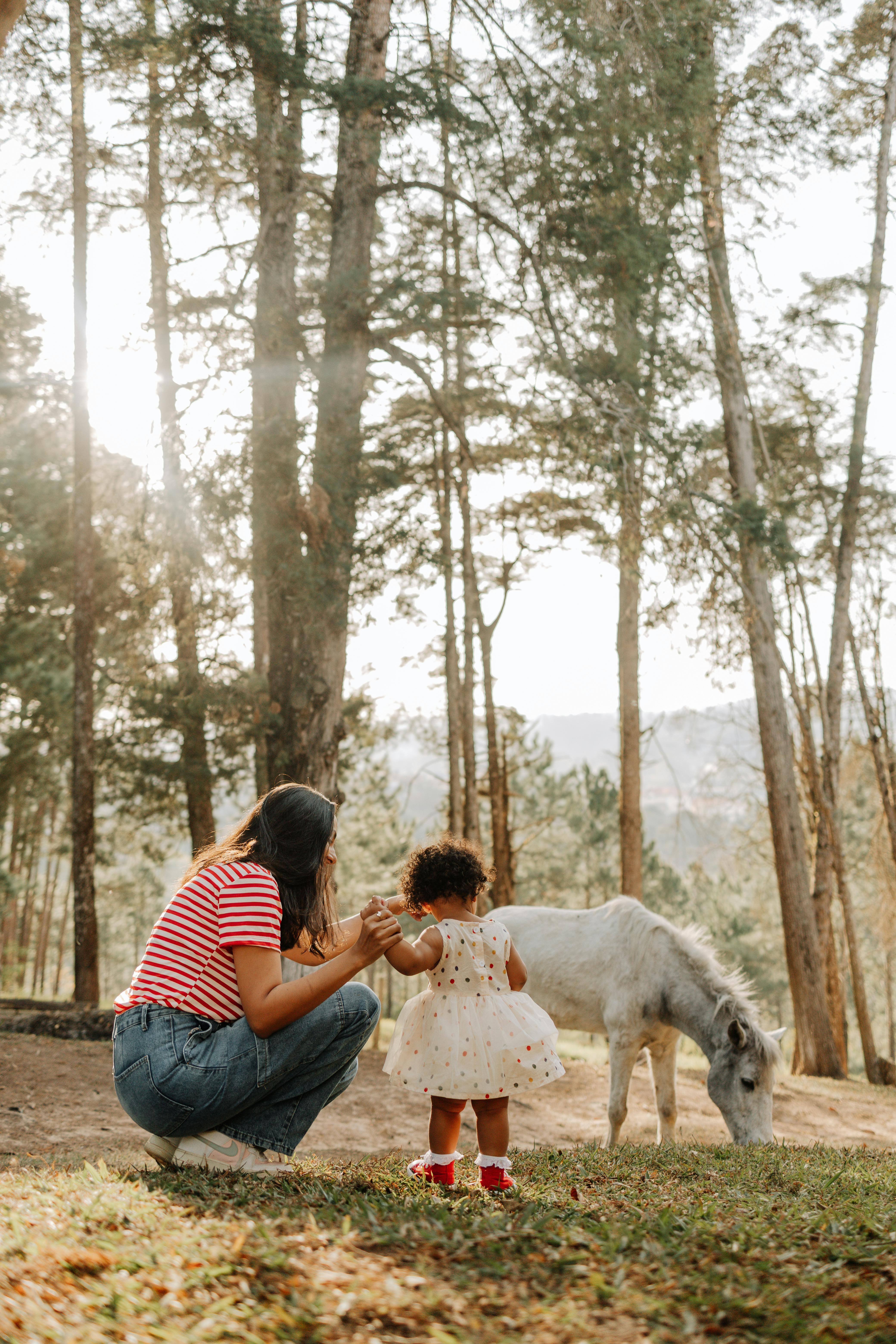 A woman holding a child's hand in front of a horse in woodland