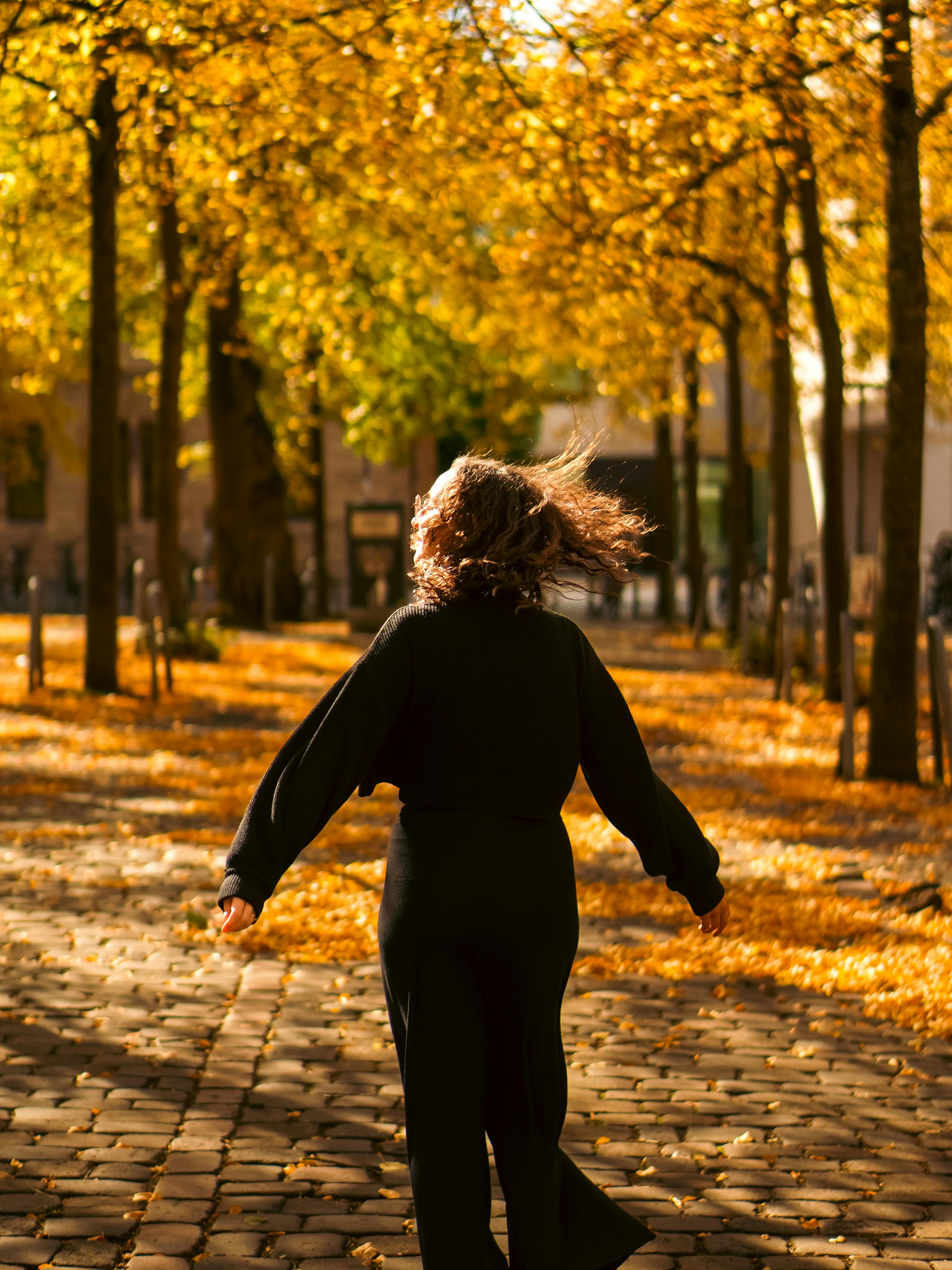 A woman with her arms slightly surrounded by trees with yellow-orange leaves